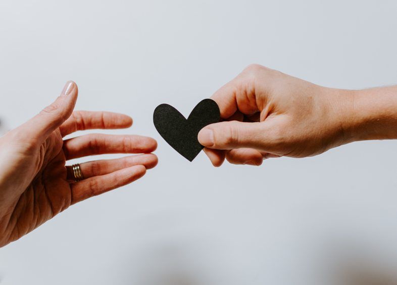 Black paper heart being handed form one person's hand to another