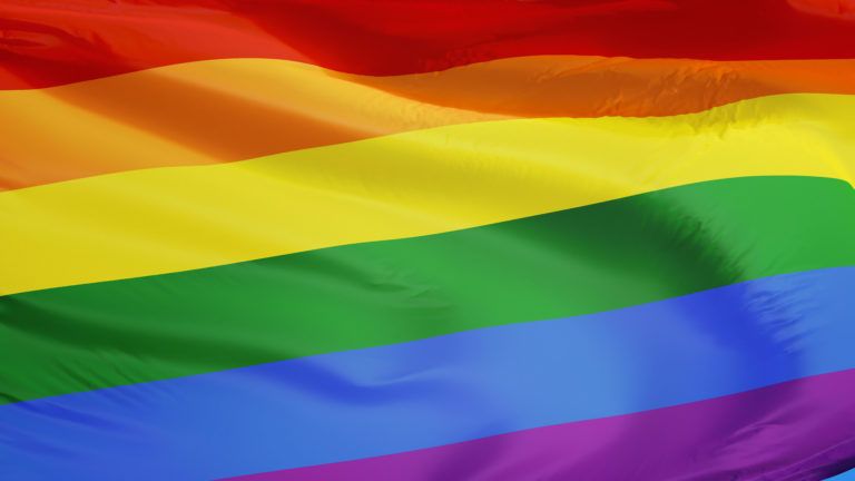 The gay pride rainbow flag waving against clean blue sky, close up ...