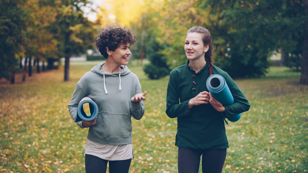 Two women walking with yoga mats in a park